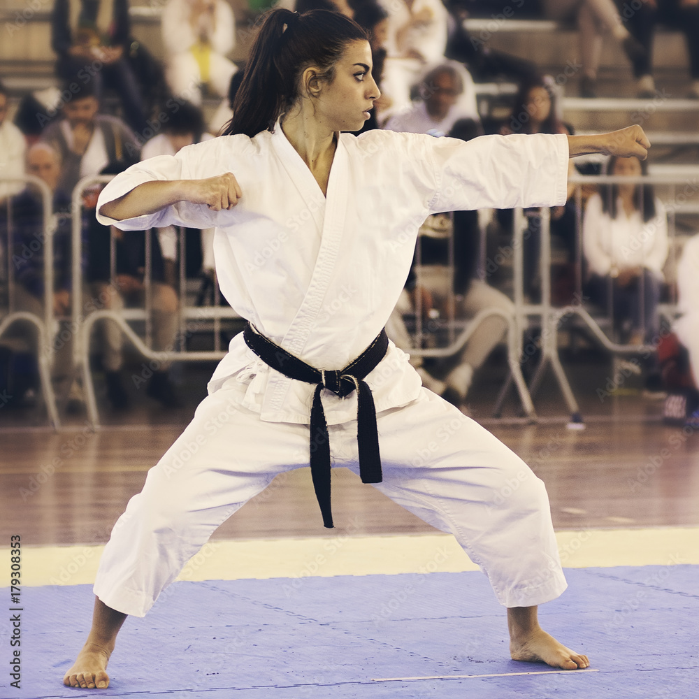 A black belt girl is performing a kata at a karate competition. People out of focus in background. A black belt girl is performing a kata at a karate competition. People out of focus in background.