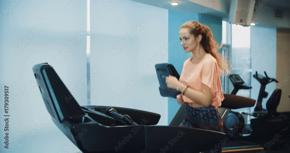 Attractive curly girl running on the treadmill in the sport gym Attractive curly girl running on the treadmill in the sport gym