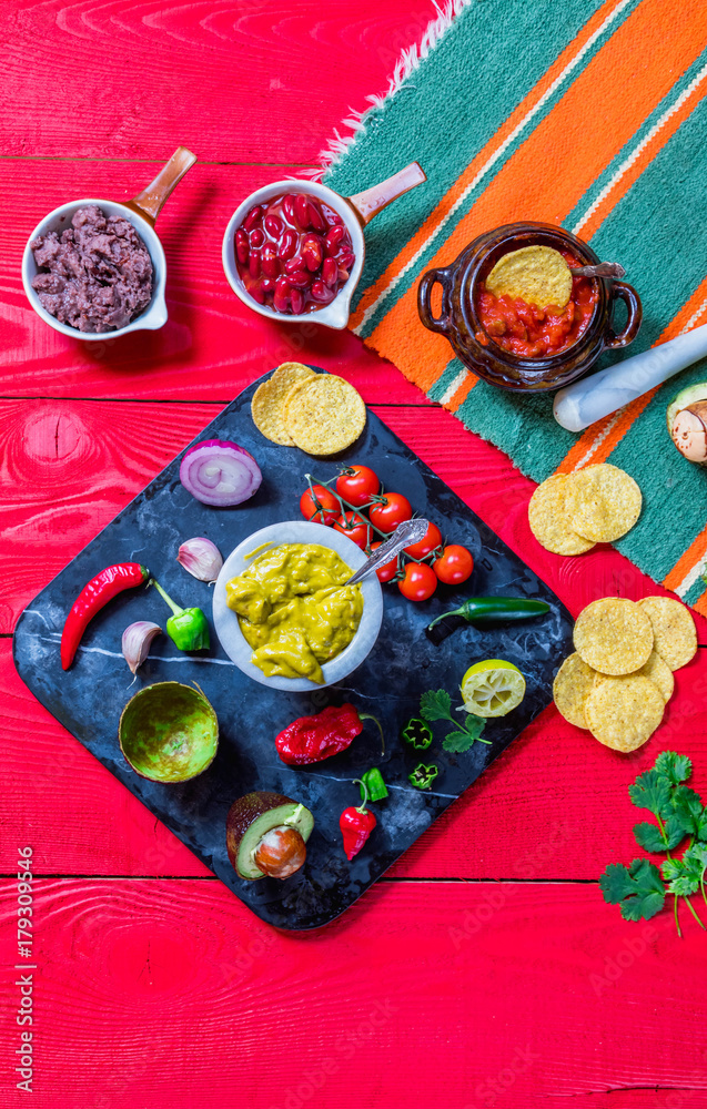 Mexican food concept:homemade guacamole, tortilla chips, salsa, chilli and fresh ingredients over vintage red rustic wooden background. Mexican food concept:homemade guacamole, tortilla chips, salsa, chilli and fresh ingredients over vintage red rustic wooden background.