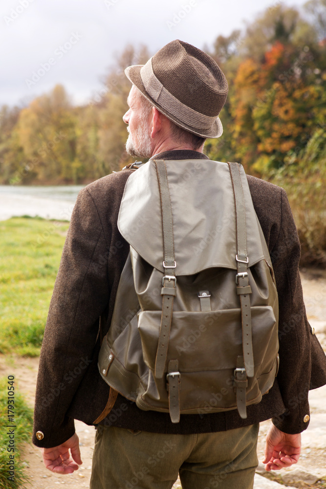 backside of bavarian man with backpack standing by river backside of bavarian man with backpack standing by river