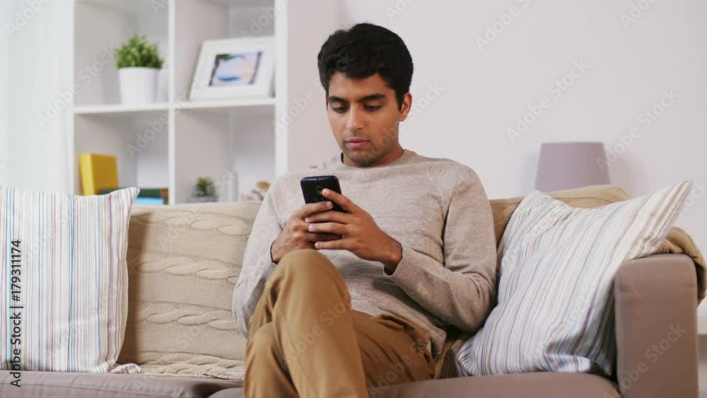 man with smartphone sitting on sofa at home