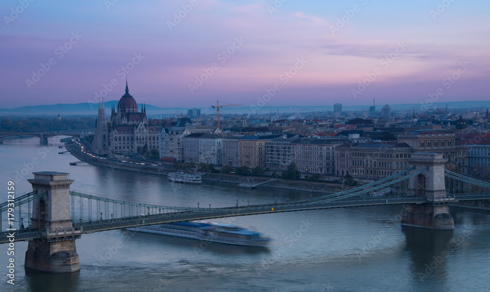 Parliament in Budapest in early morning and a big boat under the bridge  through  river Danube 