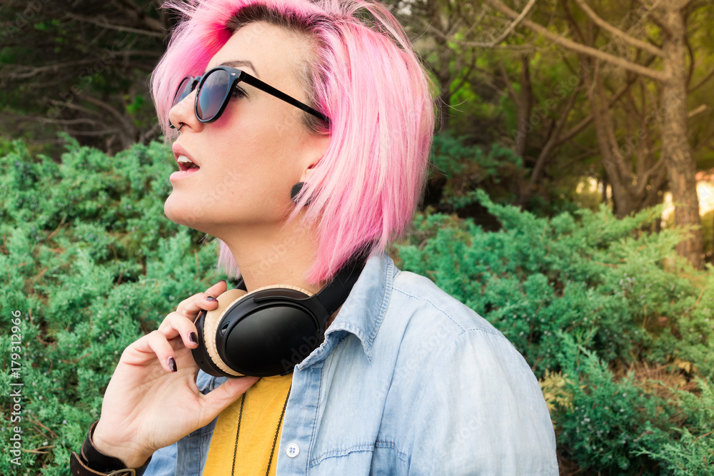 Portrait of beautiful girl sitting in park with headphones listening to music, with fuchsia hair Portrait of beautiful girl sitting in park with headphones listening to music, with fuchsia hair