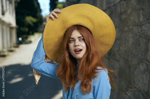 Surprised Caucasian woman holding hat near stone wall