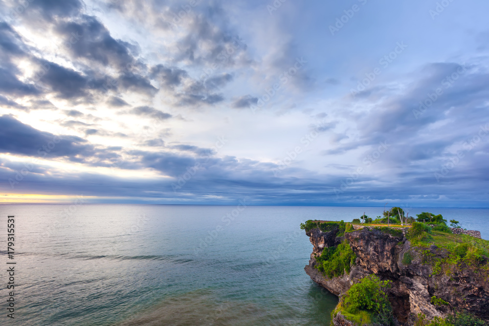 Volcanic green rock with huge stones, on the sea shore, against the backdrop of beach sunset. Beautiful blue clouds on the horizon. Balangan beach view, Jimbaran, South Kuta, Bali, Indonesia.