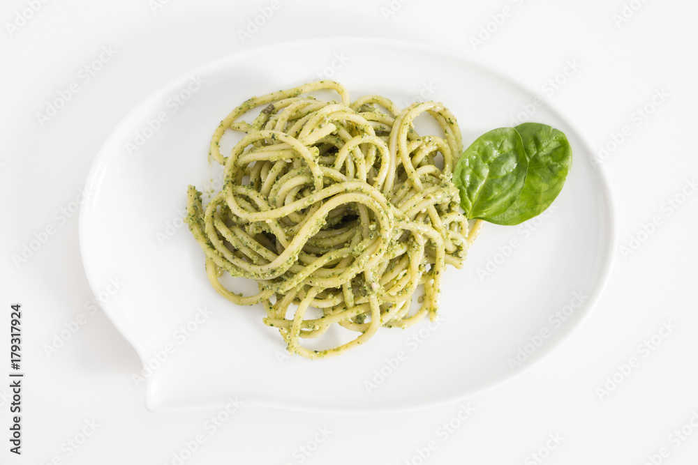 Spaghetti pasta with pesto sauce in white dish in shape of a chat bubble, on white background.