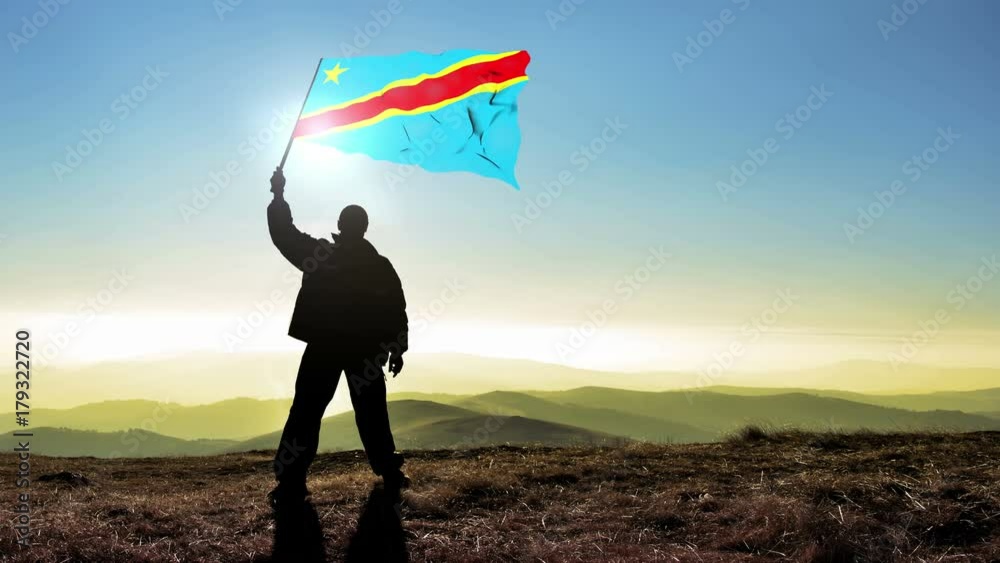 Successful silhouette man winner waving Democratic Republic of Congo flag on top of the mountain peak. Cinemagraph LOOP background
