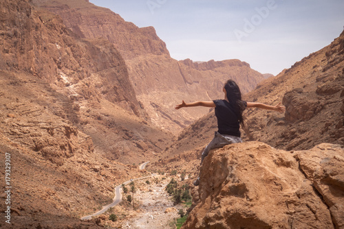 A young woman, sitting on the top of a valley, enjoying the sight and feeling happy, with her arms open. 
