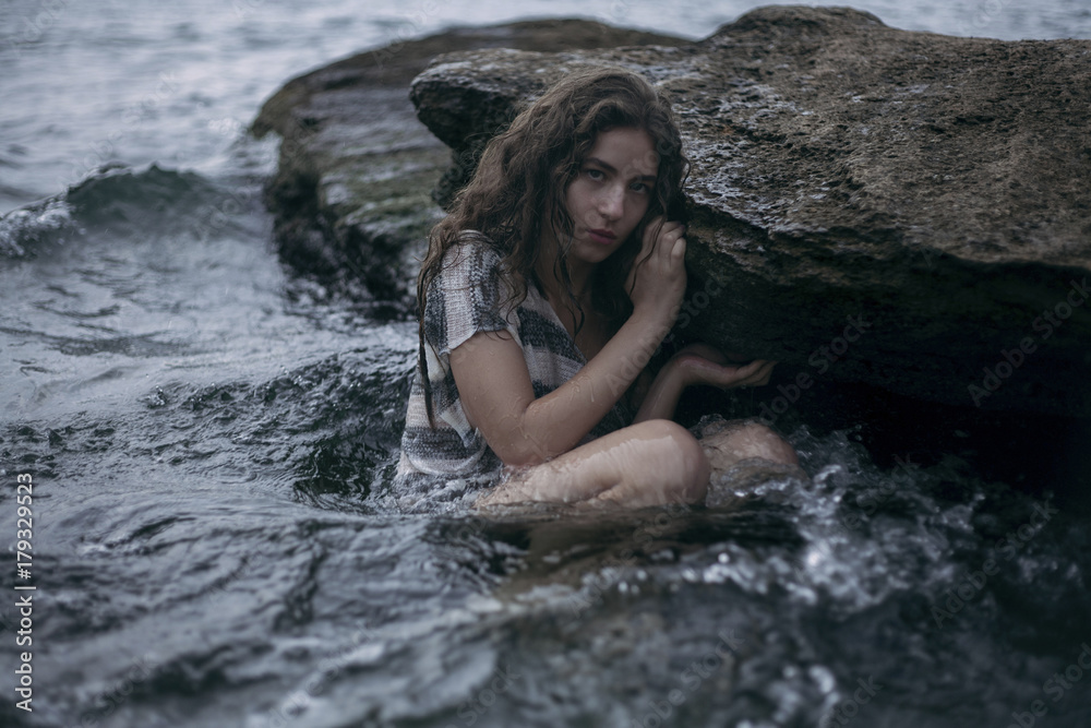 Caucasian girl sitting on rock in ocean Caucasian girl sitting on rock in ocean