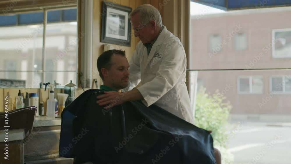 Medium slow motion panning shot of barber putting smock on customer / Pleasant Grove, Utah, United States