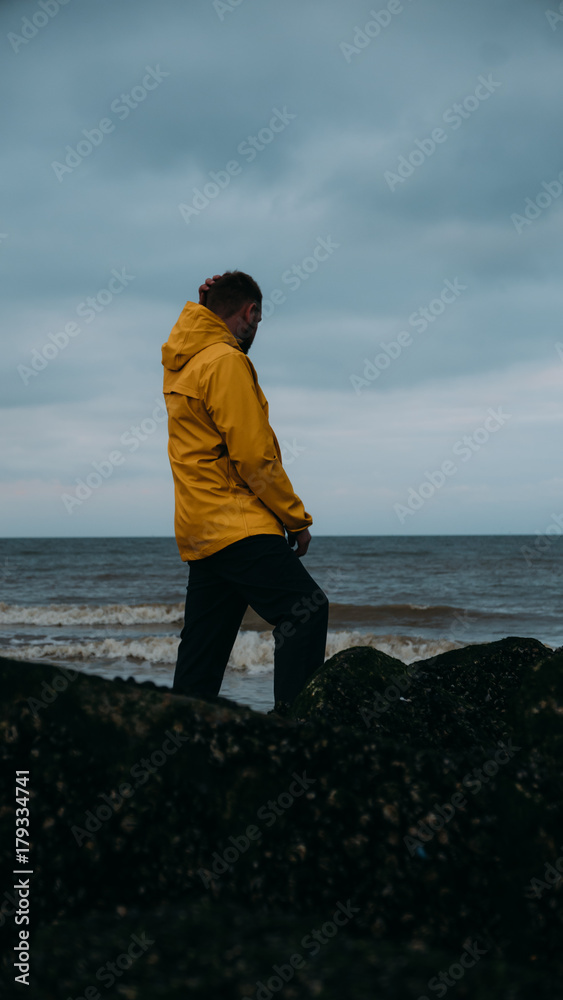 Adult Caucasian male in yellow raincoat enjoying the view of a sunset over the sea