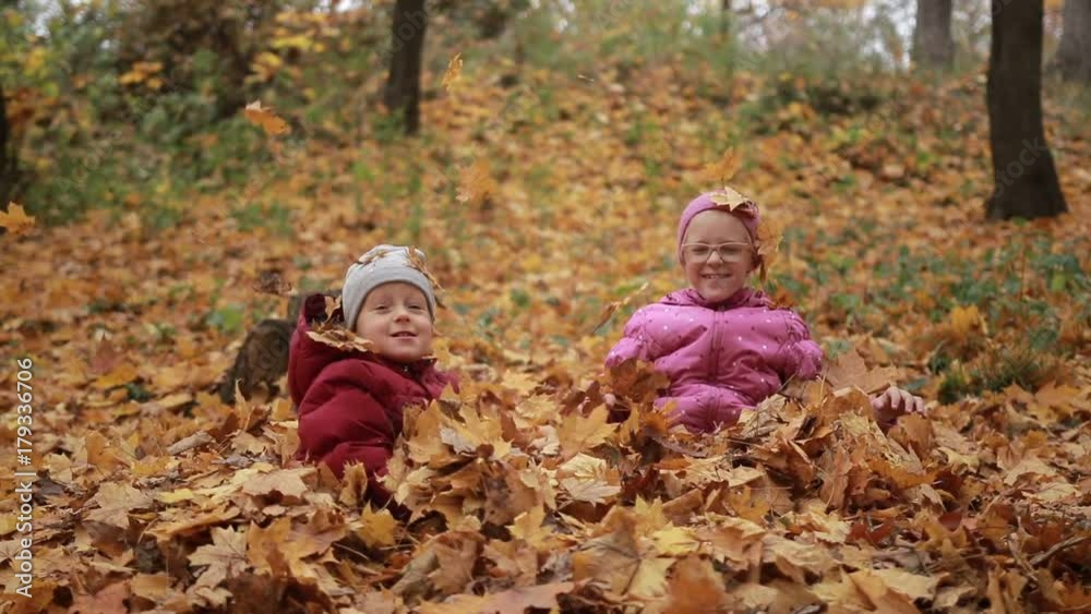 Two happy kids throwing fallen leaves up in fall