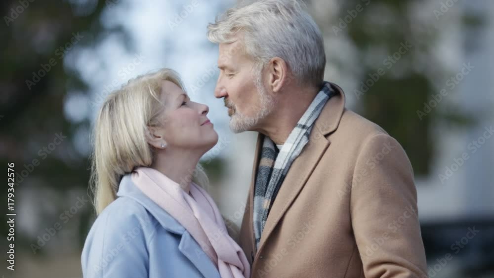 Happy mature couple share a kiss whilst walking in the city Happy mature couple share a kiss whilst walking in the city