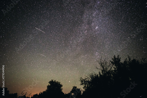 Background of bright starry night sky with lights upon on it and silhouette of trees