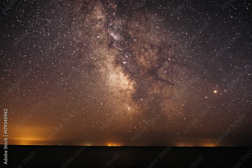 Background of bright and night-starry sky with the Milky Way upon on it and light over the water