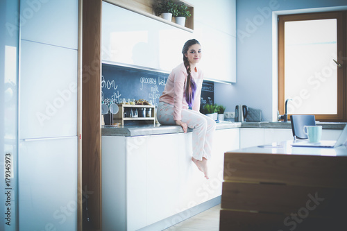 Young woman sitting on table in the kitchen.