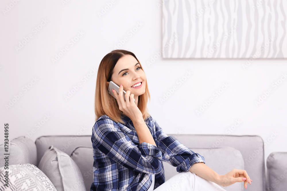Young woman using cell phone while sitting on sofa at home Young woman using cell phone while sitting on sofa at home