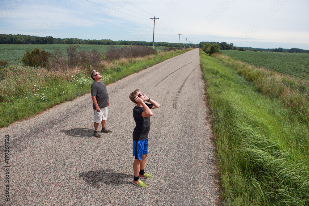 Obraz premium People looking at the sun during a solar eclipse on a country road