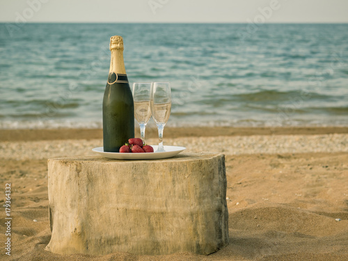Table from a piece of wood with a bottle of champagne and strawberries by the sea.