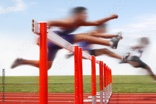 Hurdle race, men jumping over hurdles in a track and field race. Motion blurred image, digitally altered unidentifiable face. photo