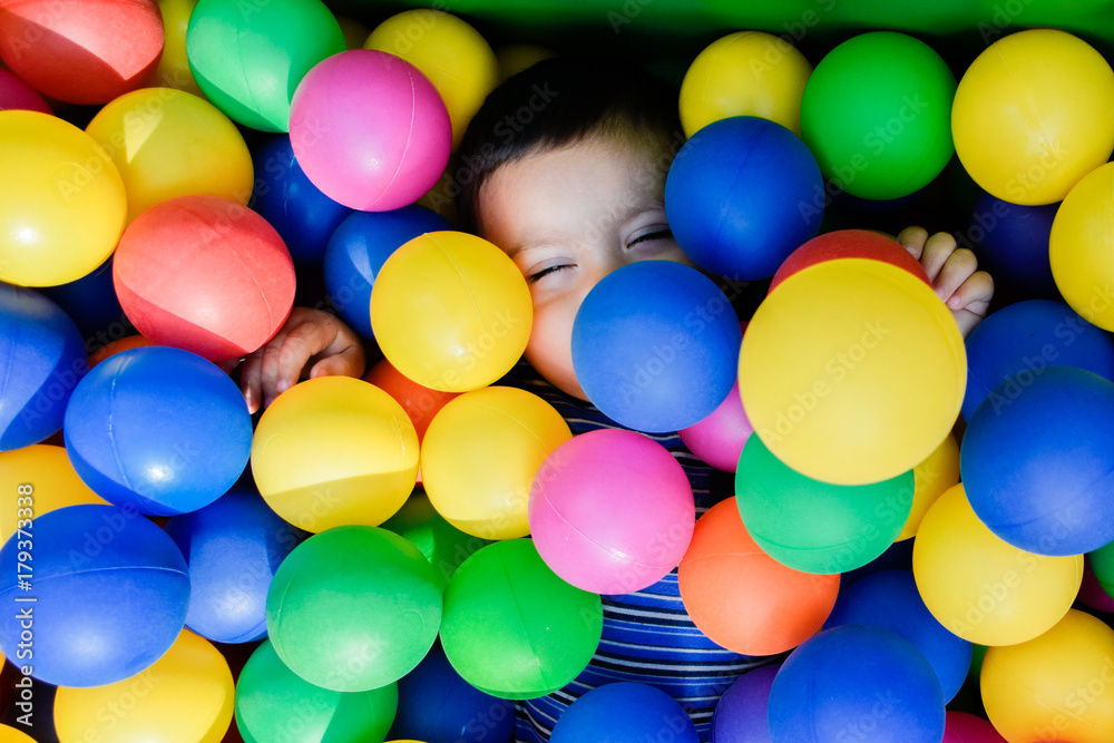 Obraz premium Happy little boy playing in the pool with colorful plastic balls.