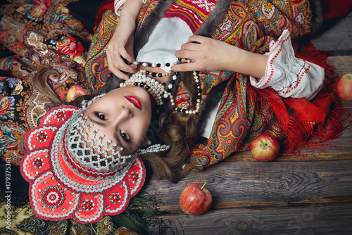 The girl in the red headdress and Russian folk style among apples on dark wooden background top view