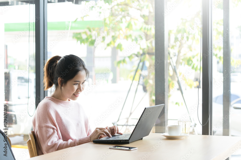 Casual young Asian girl working at a coffee shop with a laptop. female freelancer connecting to internet by computer with flare light. Woman working office. Casual young Asian girl working at a coffee shop with a laptop. female freelancer connecting to internet by computer with flare light. Woman working office.