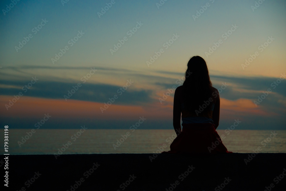 Lonely girl watching sunset near the sea or ocean