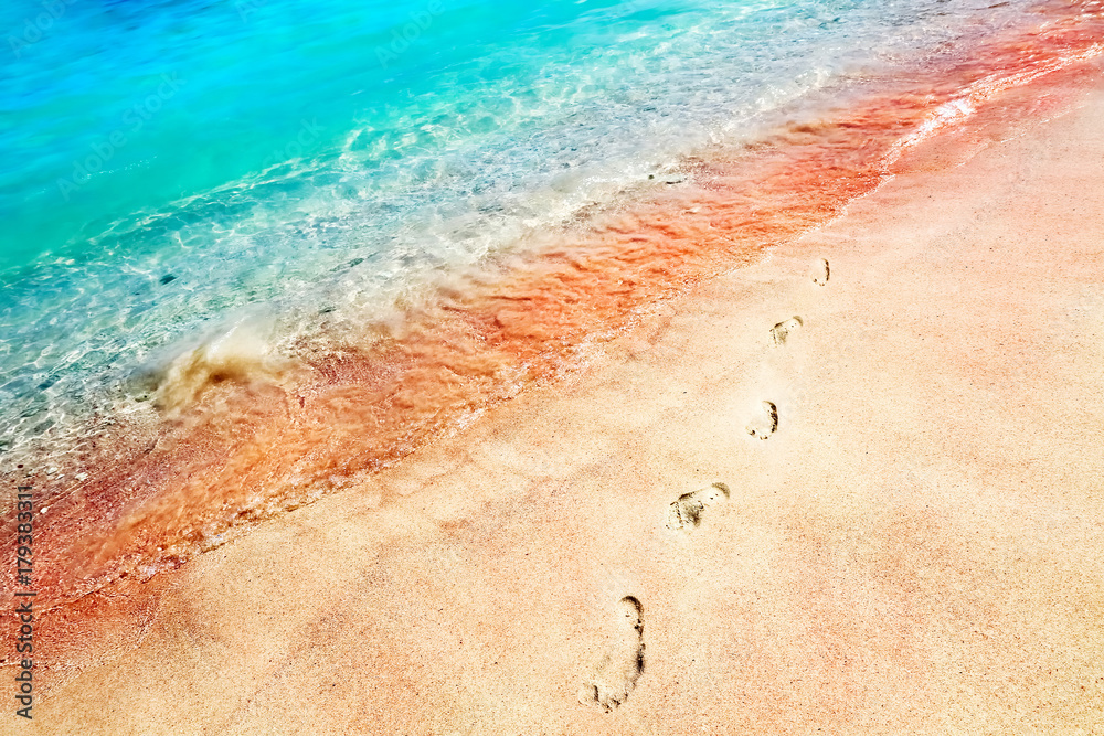 Footprints of the people on a golden pink sand on the sea coast. Soft waves of pink, red and blue color. Multicolores sea water. Marine tropical creative background close up.