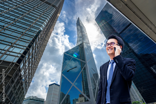 Photography Portrait of asian handsome business man using cell phone, smiling, Hong Kong downtown business district background