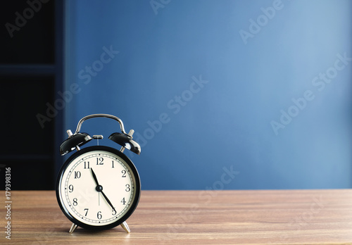 black bell clock on wood table and blue background