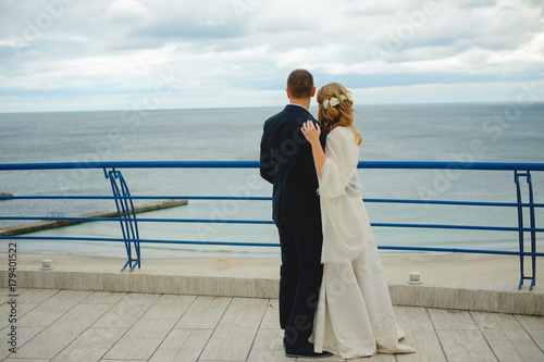 Couple in love young bride and groom dressed in white hugging on cliff background of blue sea in their wedding day