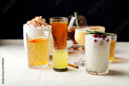 Set of various winter cocktails: mulled wine, eggnog, limoncello, old-fashioned, coconut margarita. Black background, white linen tablecloth.