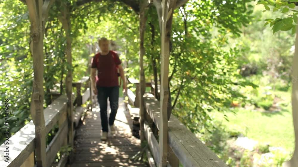 male traveler walking along a wooden bridge in the park male traveler walking along a wooden bridge in the park