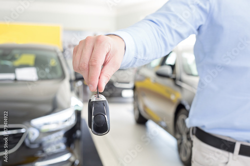 male adult dealer hand giving car keys, close-up photo taken indoors, cars at the background © Zdenka