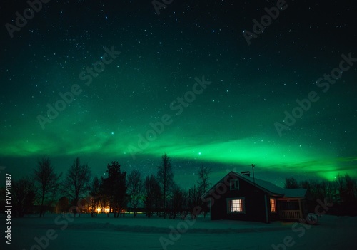 Northern lights (Aurora Borealis) over cottage in Lapland village. Finland