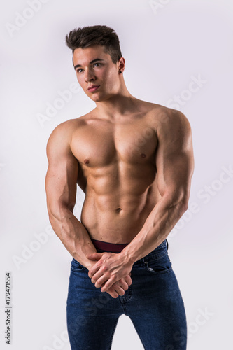 Handsome young muscular man shirtless wearing jeans, on light background in studio shot