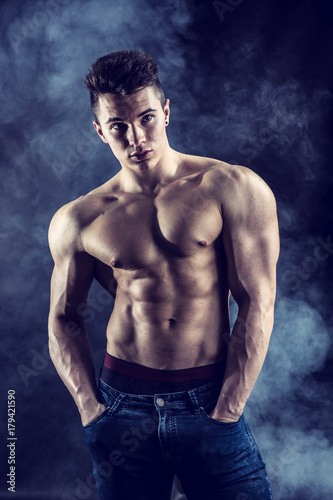 Handsome young muscular man shirtless wearing jeans, on dark background in studio shot © theartofphoto