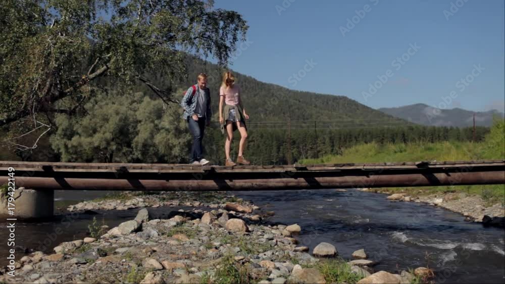 a pair of travelers sit on a bridge across a mountain river a pair of travelers sit on a bridge across a mountain river