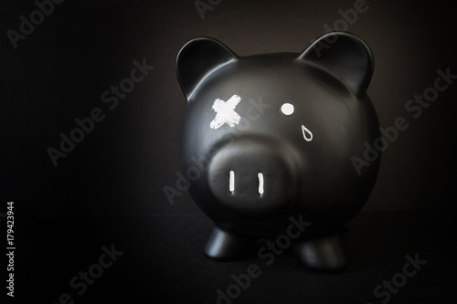 Black piggy bank with a tear and X'd out eye, taking a beating