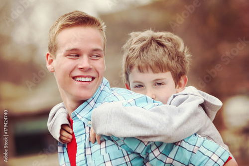 Older brother giving young boy a piggyback ride outdoors smiling photo