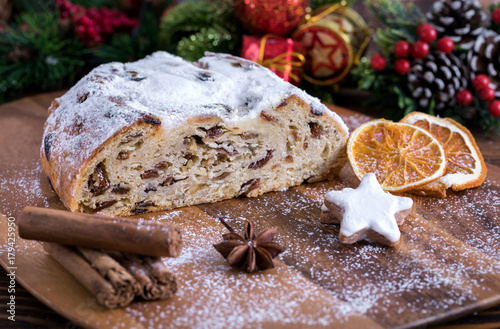 Weihnachtlicher Butterstollen mit Rosinen auf Holztisch mit Gewürzen und Puderzucker photo