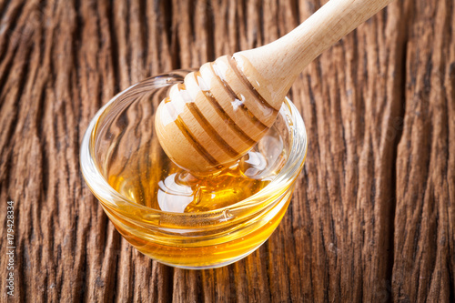 Honey bowl with dipper and flowing honey on the wood table