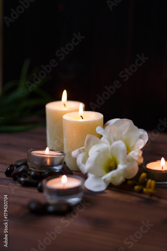 A candle in a glass vase, decoration and various interesting elements on a dark wooden background. Candles burning. Set for spa and massage. stones for massage