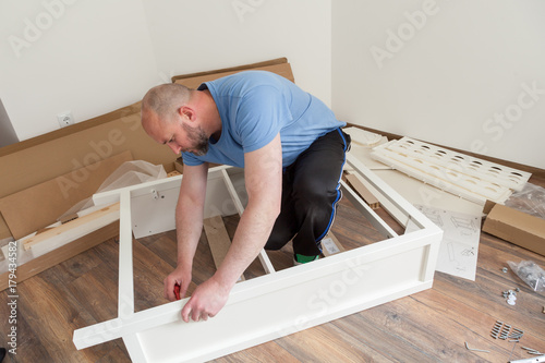 Man dressed casual assembling furniture in new house. Carpenter repair and assembling furniture at home photo