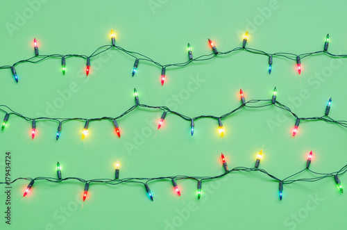 Christmas light bulbs on pattern strings in multi colours  blue  yellow  pink   red on green background with copy space for Christmas text decor  new year or event celebration  ornament concept