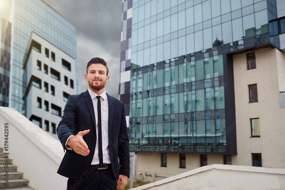 Businessman extends a hand for a handshake against a business building background. Businessman extends a hand for a handshake against a business building background.