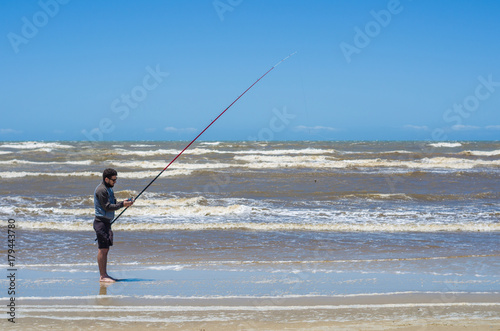 Jovem homem pescando na praia.