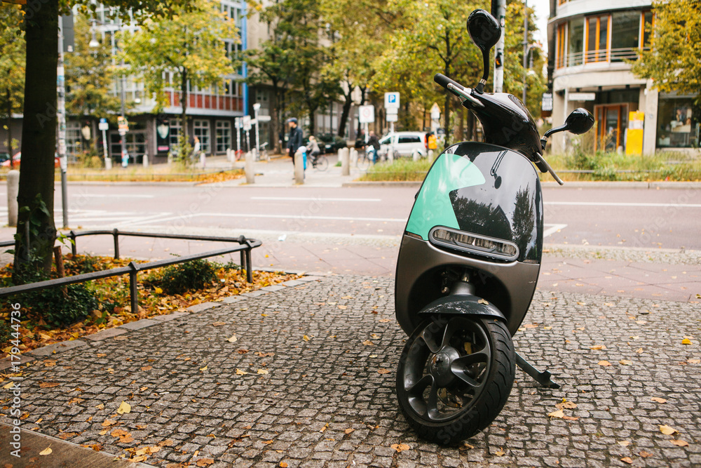 A popular vehicle in the city is called an electric scooter. In the background a street in Berlin.