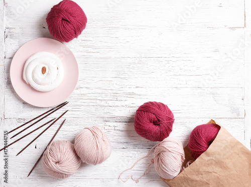 Paper bag with yarn, knitting needles and pink plate with cake on a white wooden background. photo